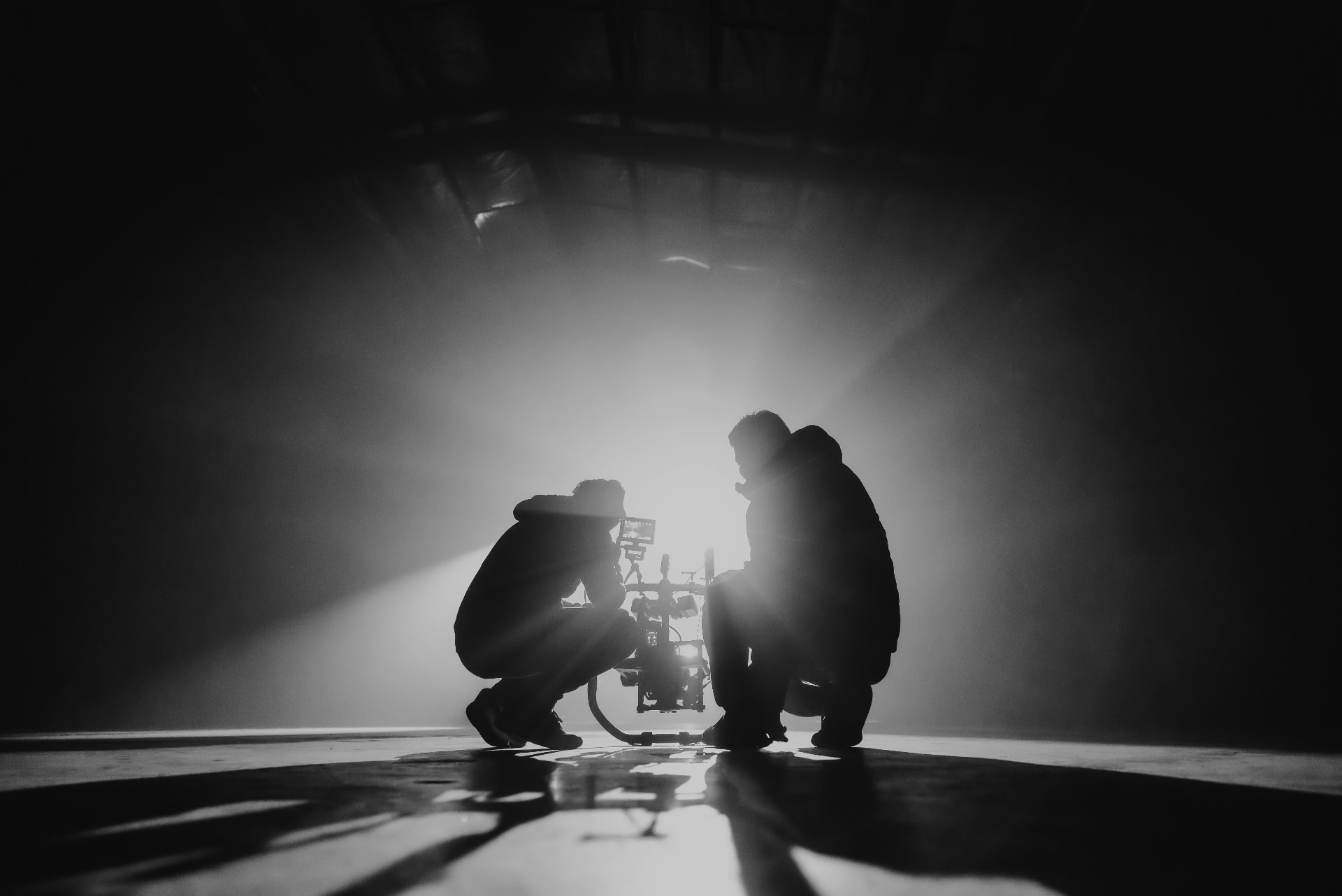 Silhouetted camera crew at work in a dark studio, lit from behind