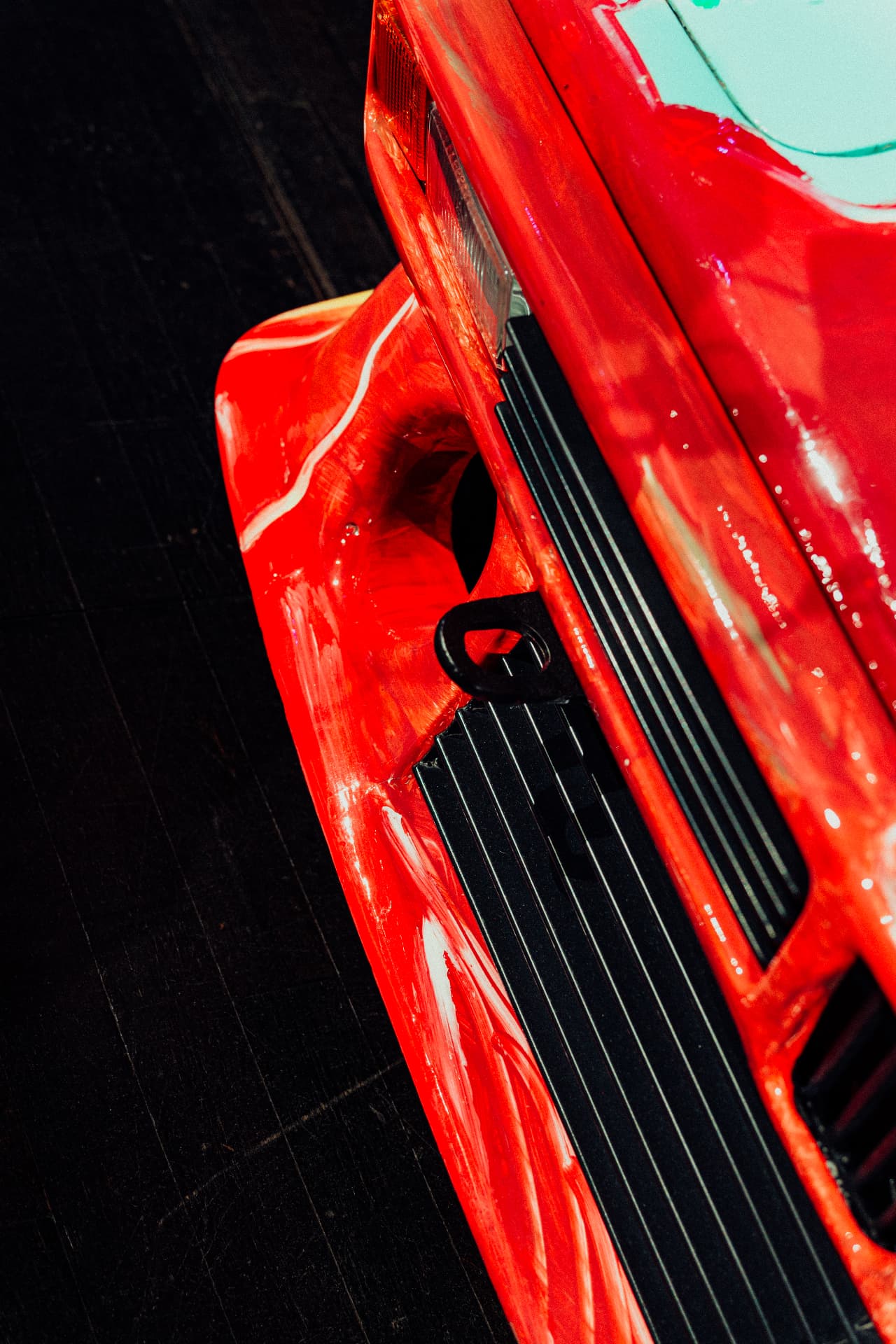 Detail of a glossy red BMW Art Car body with painted strokes, taillight and black side grille