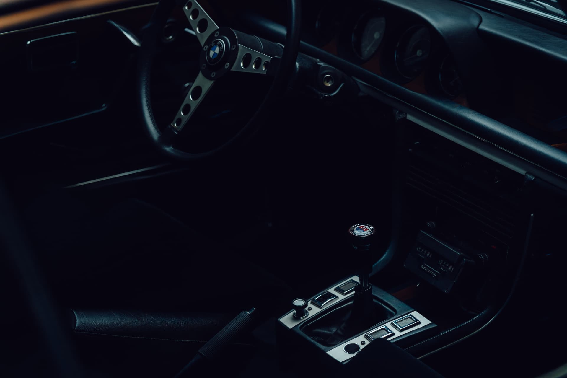 Dark cockpit of a classic BMW with steering wheel, gear shift and chrome switchgear