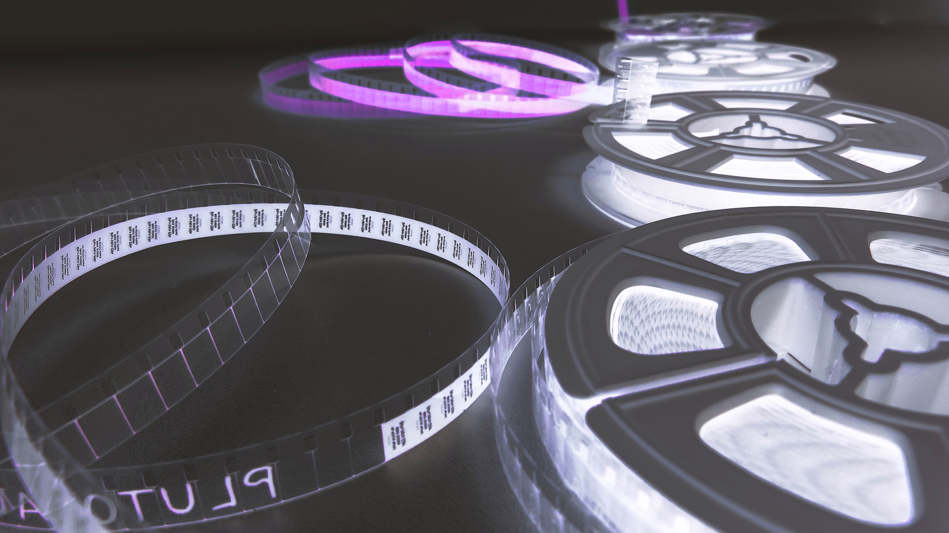 Illuminated film reels and film strip glowing with purple light in the dark