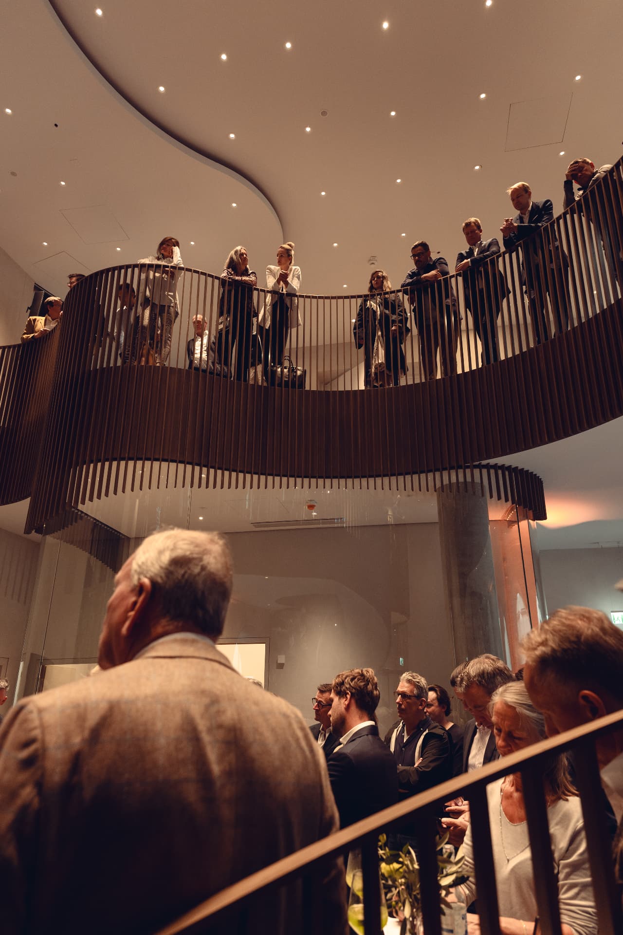 View up the curved atrium balcony of Herzog Max with guests overlooking the opening ceremony