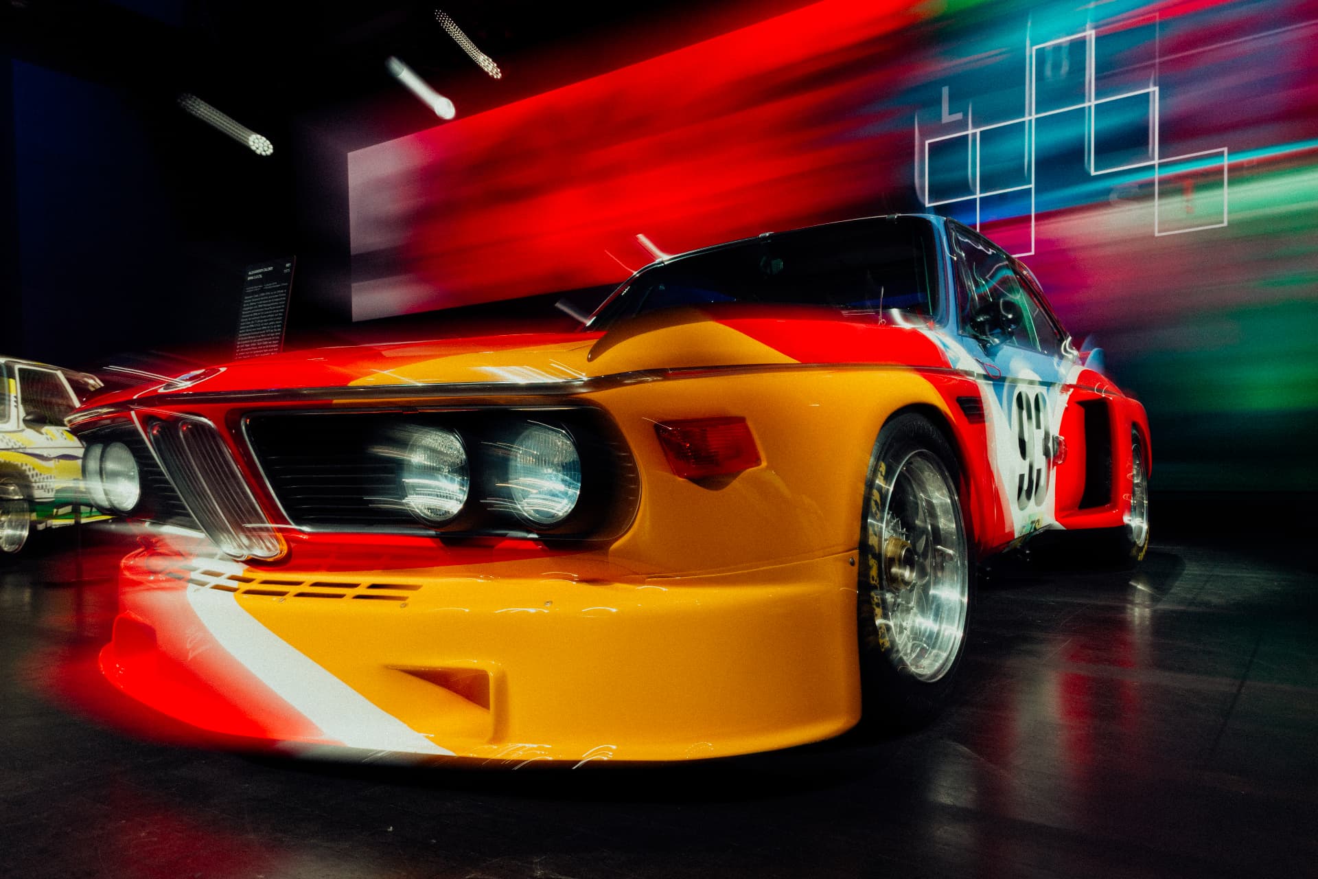 Orange and red BMW Art Car photographed from a low angle with vivid light trails at BMW Welt