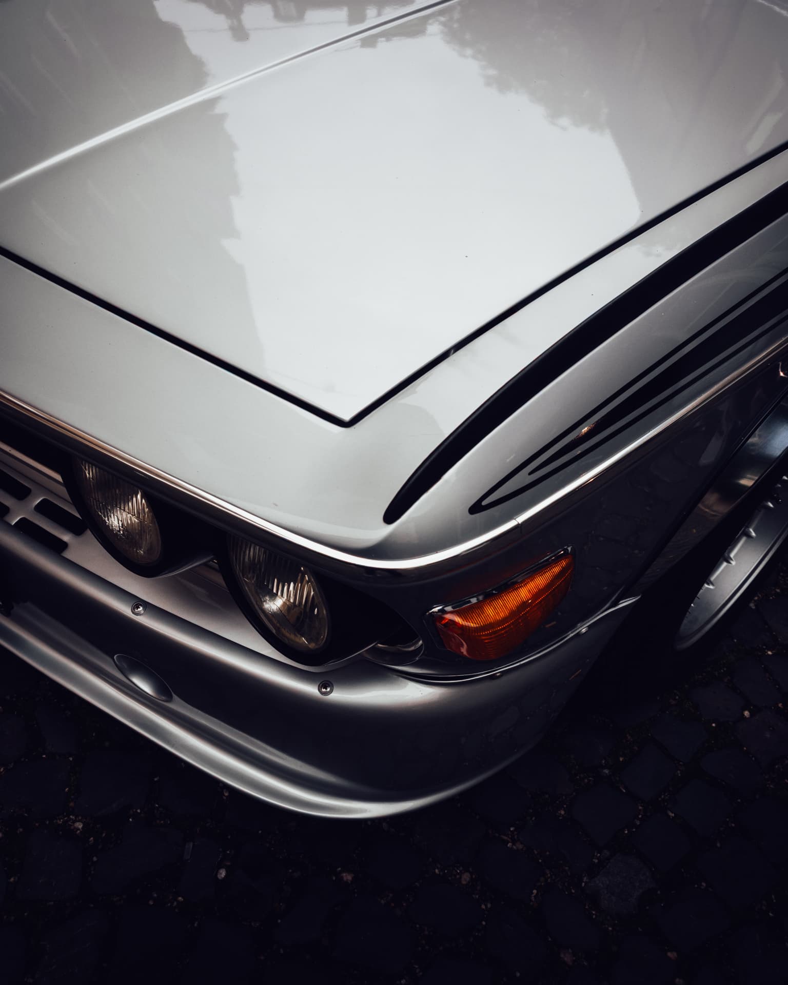 Close-up of the white bonnet, headlight and chrome bumper of a classic BMW in the rain