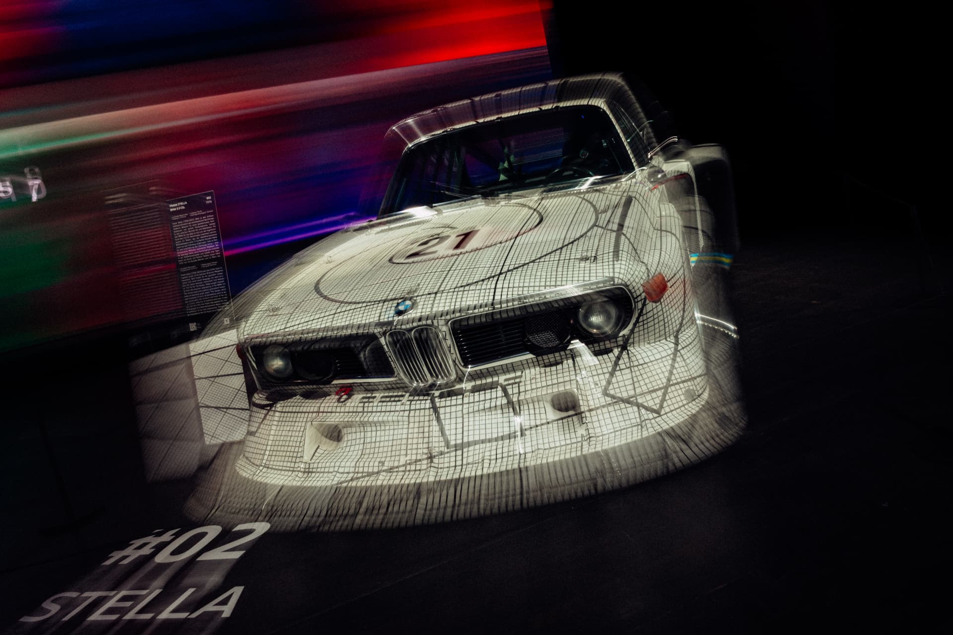 White BMW Art Car with a black grid design photographed with long-exposure light trails at BMW Welt