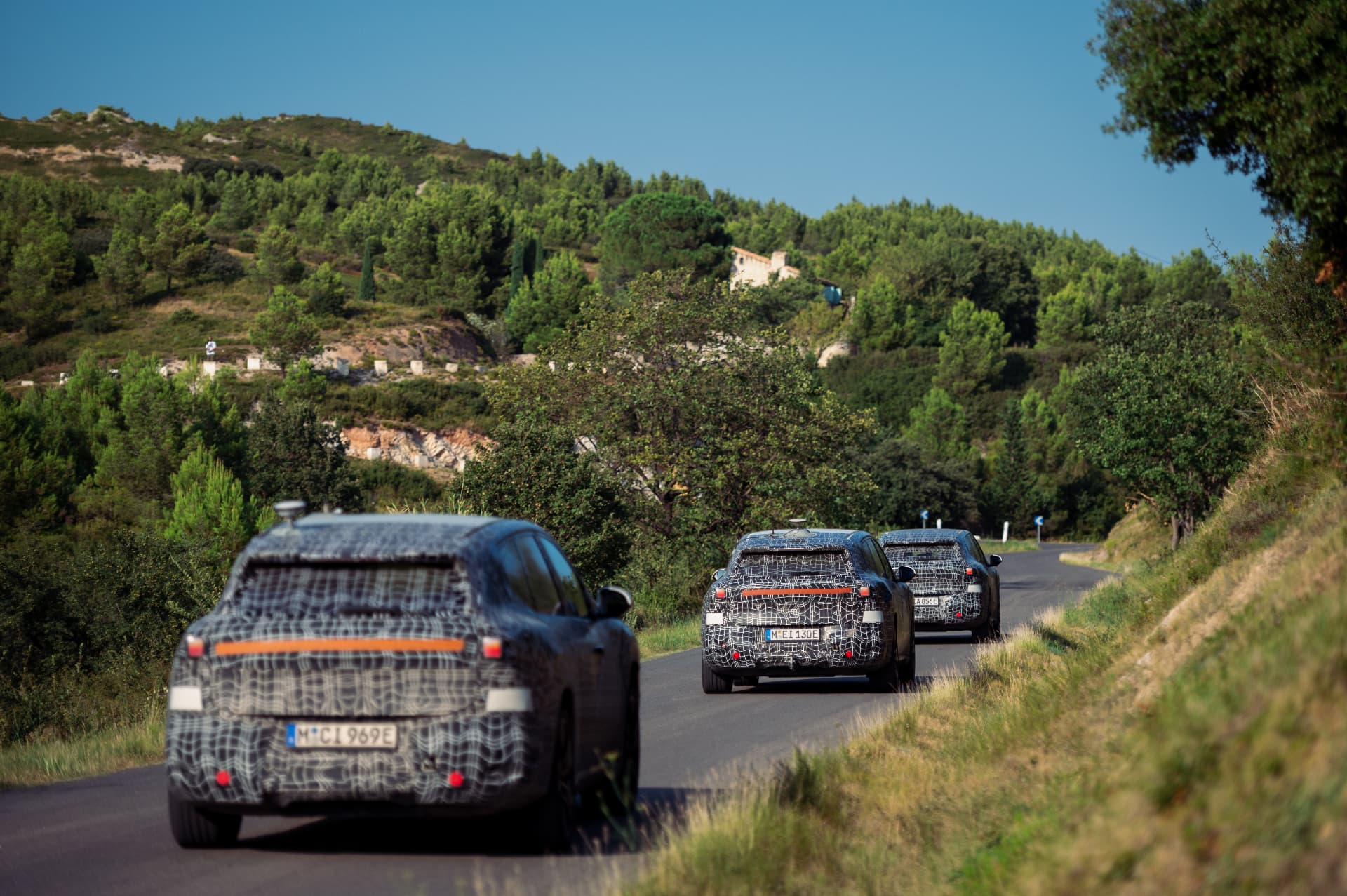 Camouflaged BMW iX3 prototypes driving in convoy on a mountain road during testing