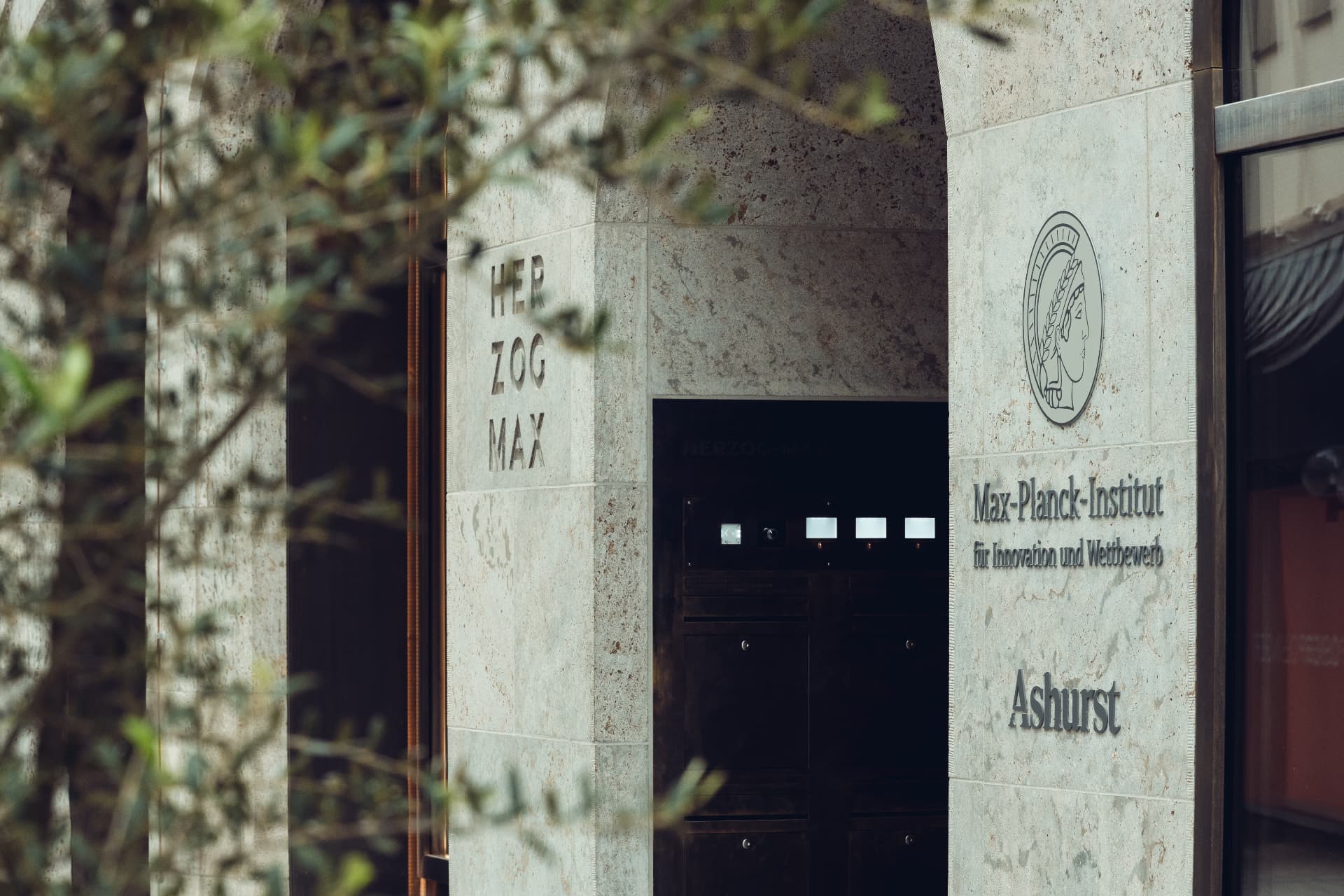 Entrance detail of Herzog Max — engraved HERZOG MAX lettering and Max-Planck-Institut signage in the stone facade