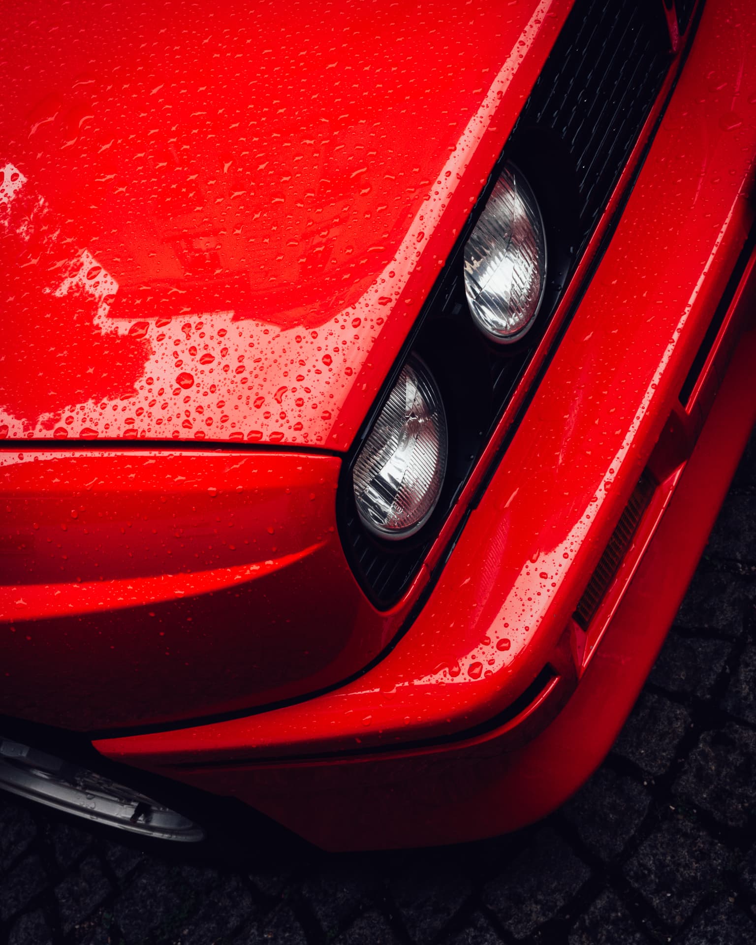 Red classic BMW bonnet with dual round headlights covered in rain drops