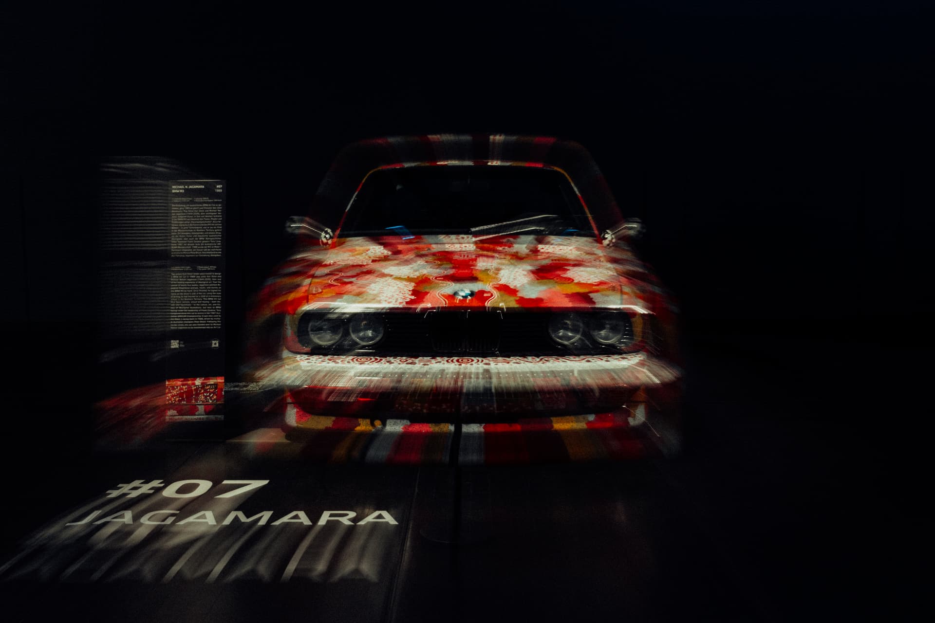 Front view of the red BMW Art Car number 07 in a dark exhibition setting at BMW Welt