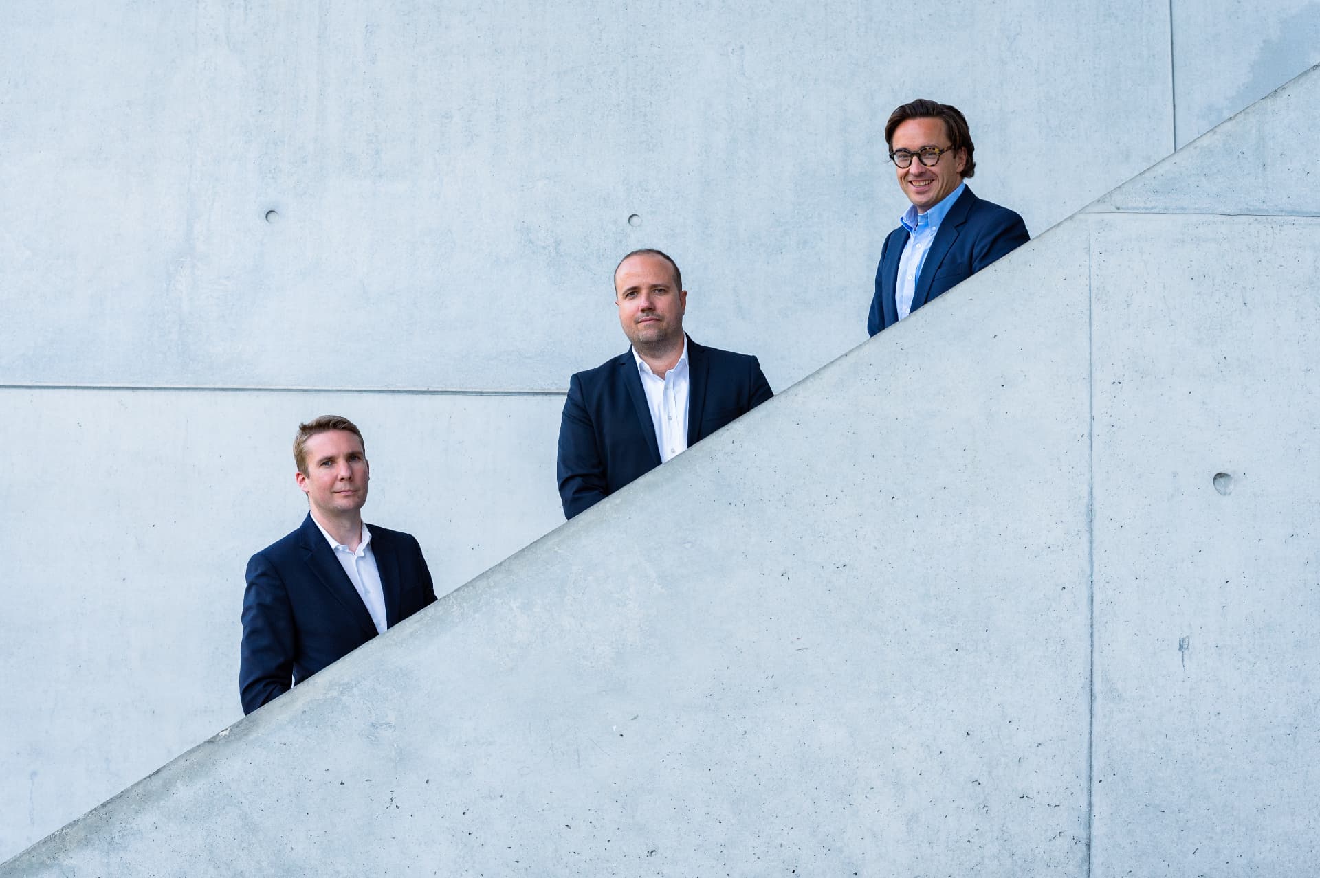 Three DMR Legal lawyers in dark suits standing on a diagonal concrete staircase