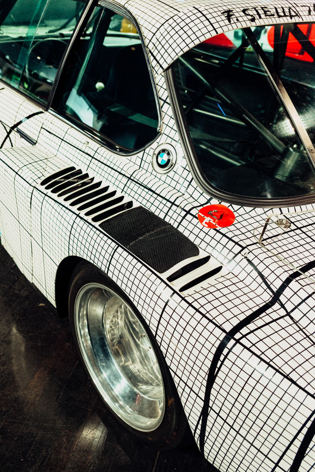 Portrait detail of the black grid pattern, wheel and side window of a white BMW Art Car
