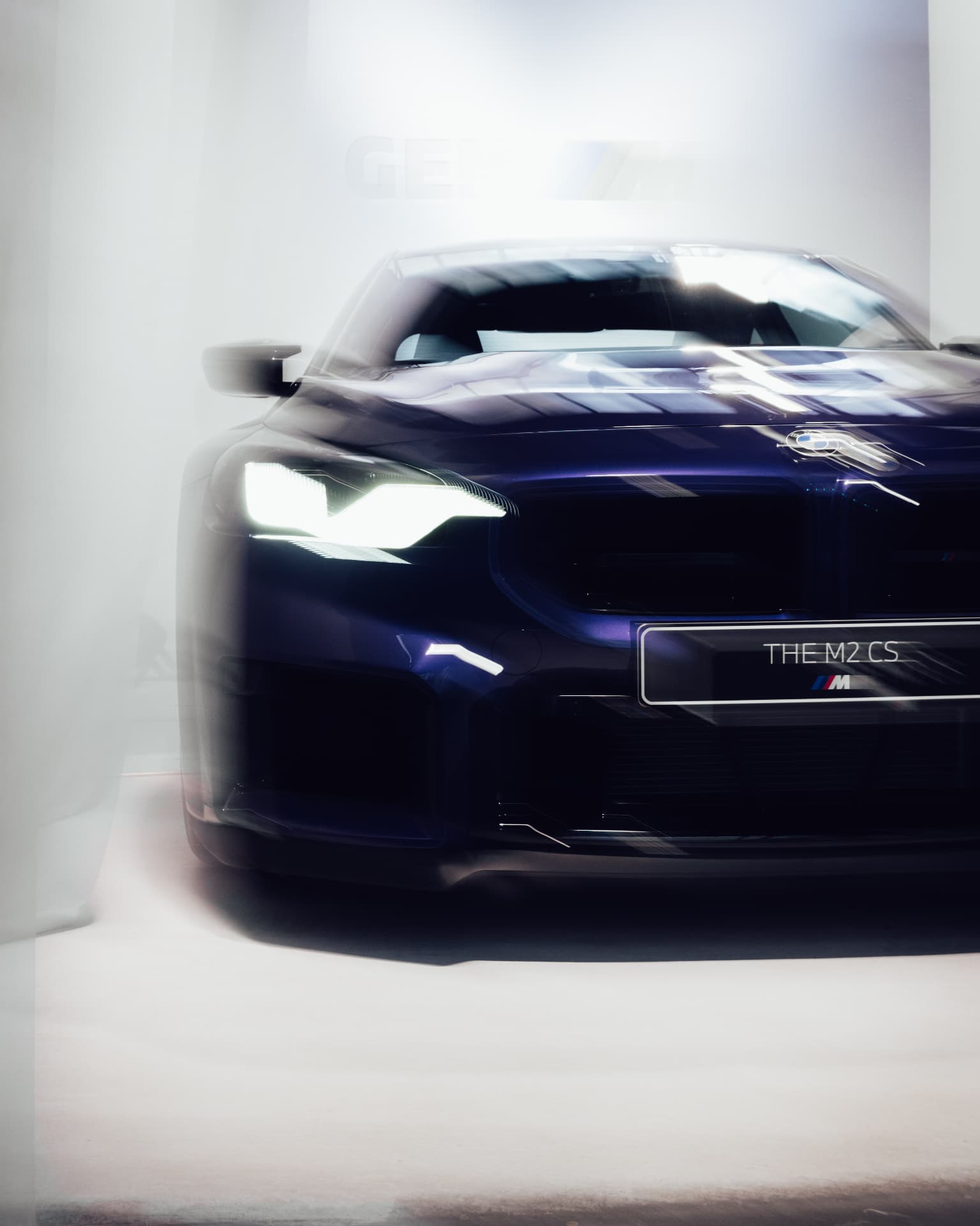 Front view of THE M2 CS in deep blue behind translucent curtain fabric at IAA 2025