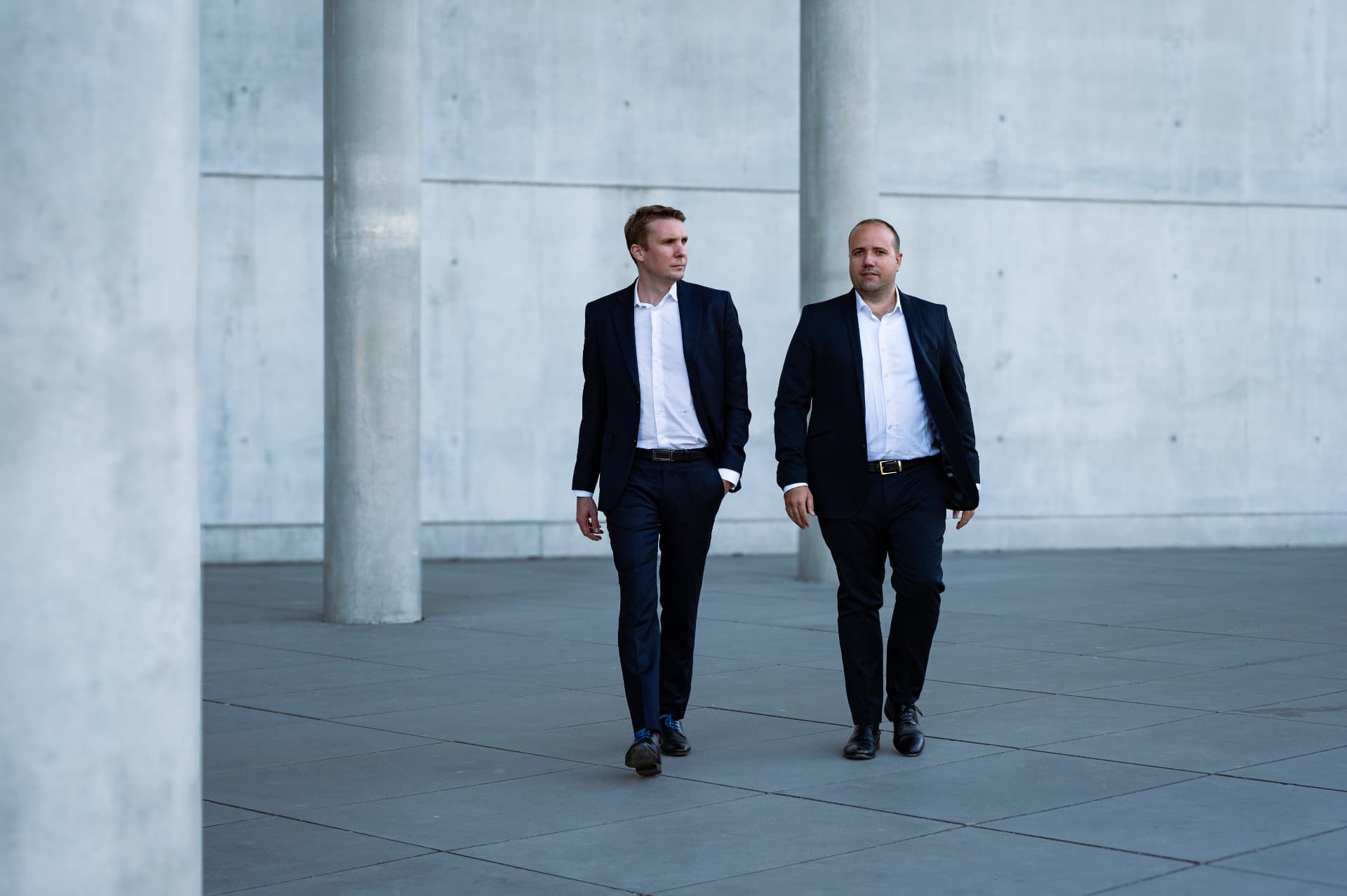 Two DMR Legal lawyers walking side by side across a paved concrete colonnade