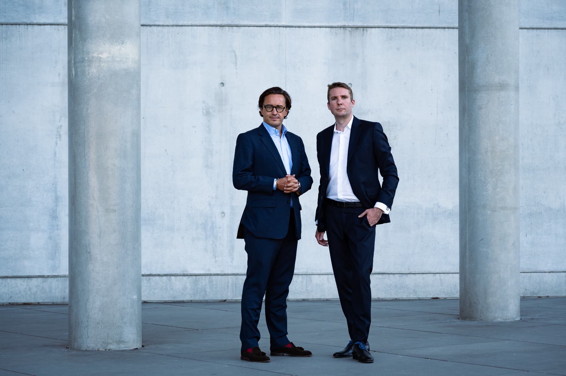 Two DMR Legal lawyers standing between concrete columns in front of a bare concrete wall