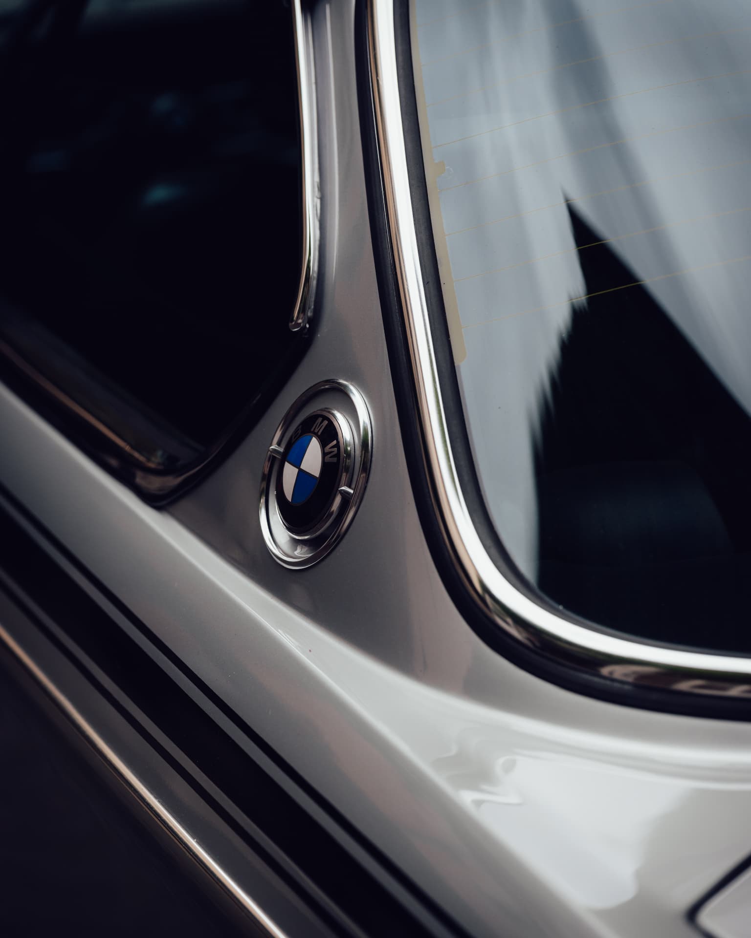 Rear C-pillar of a classic BMW with the roundel badge and rear window in the rain